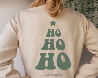 May include: A beige sweatshirt with a green Christmas tree design on the back. The tree is made up of the word "HO" repeated three times in a retro font. The text "Merry Christmas" is printed below the tree.