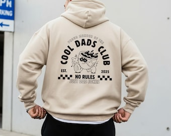 May include: Beige hoodie with a hood and long sleeves. The back features a black graphic that reads "COOL DADS CLUB" with a cartoon coffee cup design and the text "NO RULES JUST DAD JOKES".