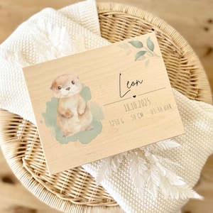 Könnte beinhalten: Holztafel mit einer Illustration eines Otters und dem Namen "Leon". Sie zeigt das Datum, das Gewicht (3250 g), die Größe (50 cm) und die Geburtszeit (03:30 UHR). Die Tafel hat dekorative Blätter.