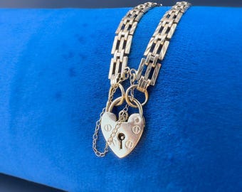 May include: A gold heart-shaped padlock charm attached to a gold chain bracelet. The bracelet is made of a linked chain design.