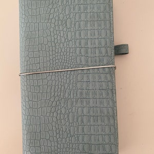 May include: A light blue leather planner with a crocodile embossed pattern and a silver closure.