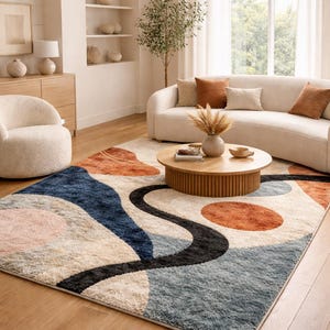 Peut inclure: Un tapis moderne avec un motif abstrait. Le tapis présente un fond crème avec des formes bleues, orange, roses et noires. Le tapis est placé dans un salon avec un canapé, une chaise et une table basse.