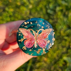 May include: A teal green resin cabochon with gold flakes and a pink butterfly design.