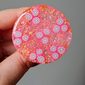 May include: A pink and white resin coaster with a glittery finish and a pattern of white circles with black dots inside.