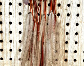 May include: A handcrafted dreamcatcher with a woven web design, adorned with feathers and beads. The dreamcatcher features a brown hoop, orange accents, and hanging feathers. The feathers are a mix of white and brown. The dreamcatcher is approximately 10 inches in diameter.