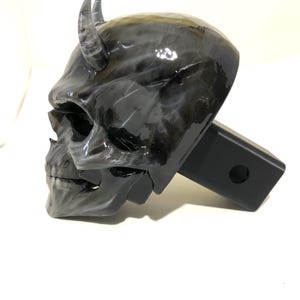 May include: Black and white skull hitch cover with horns. The skull is detailed and has a glossy finish. The hitch cover is made of durable metal and is designed to fit standard 2-inch receiver hitches.