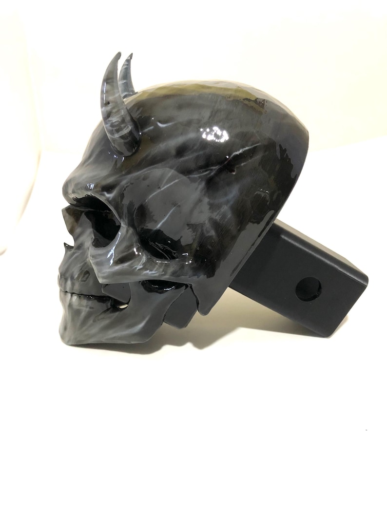 May include: Black and white skull hitch cover with horns. The skull is detailed and has a glossy finish. The hitch cover is made of durable metal and is designed to fit standard 2-inch receiver hitches.