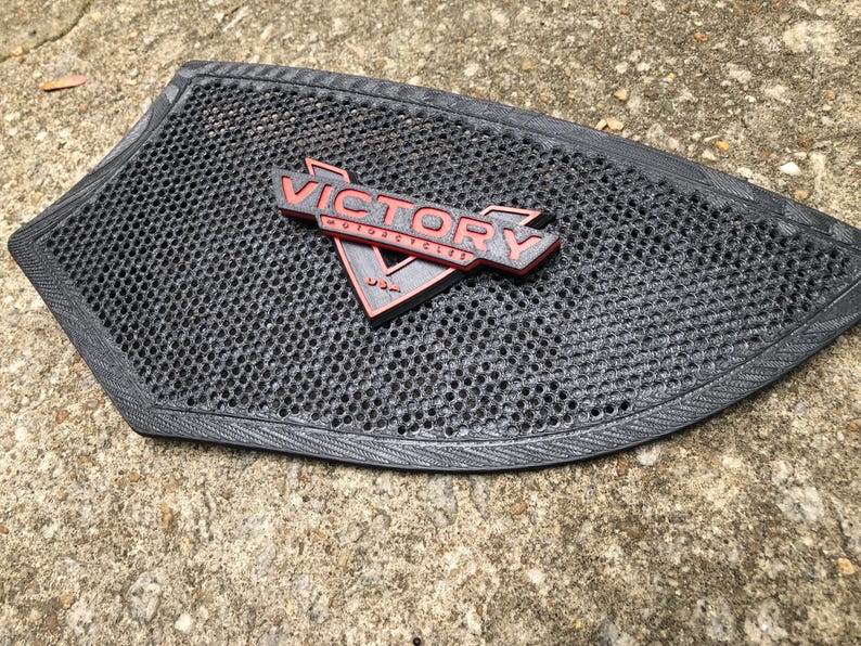 Puede incluir: Un asiento de motocicleta negro con un logotipo de Victory Motorcycles negro y rojo. El asiento tiene un patr&oacute;n de panal.