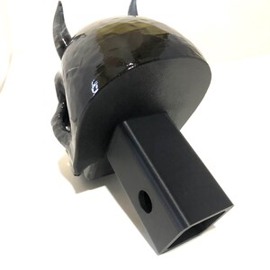 May include: Black 3D printed devil skull hitch cover. The skull has horns and a detailed face. The hitch cover is attached to a black metal hitch receiver.