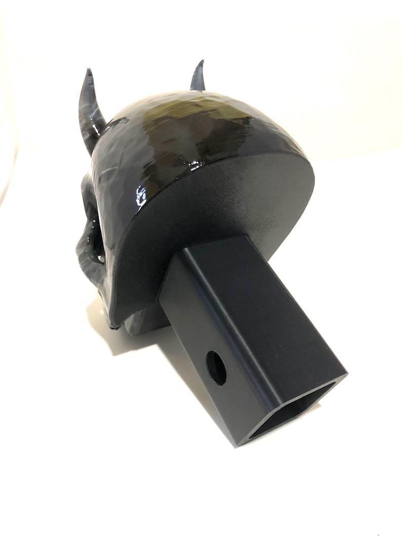 May include: Black 3D printed devil skull hitch cover. The skull has horns and a detailed face. The hitch cover is attached to a black metal hitch receiver.