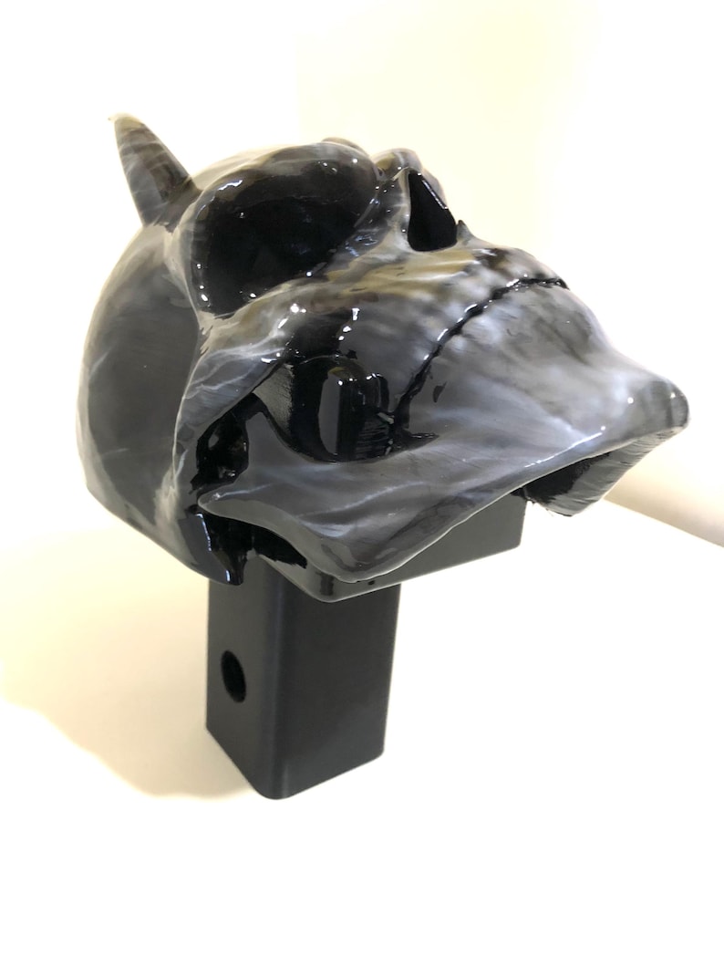 May include: A black and white skull hitch cover with a single horn. The skull is detailed with a black and white marbled paint effect. The hitch cover is attached to a black metal hitch receiver.