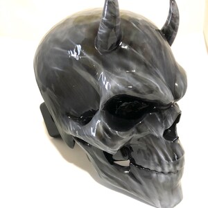 May include: A black and white skull mask with horns. The mask is made of a smooth, glossy material and has a detailed design.