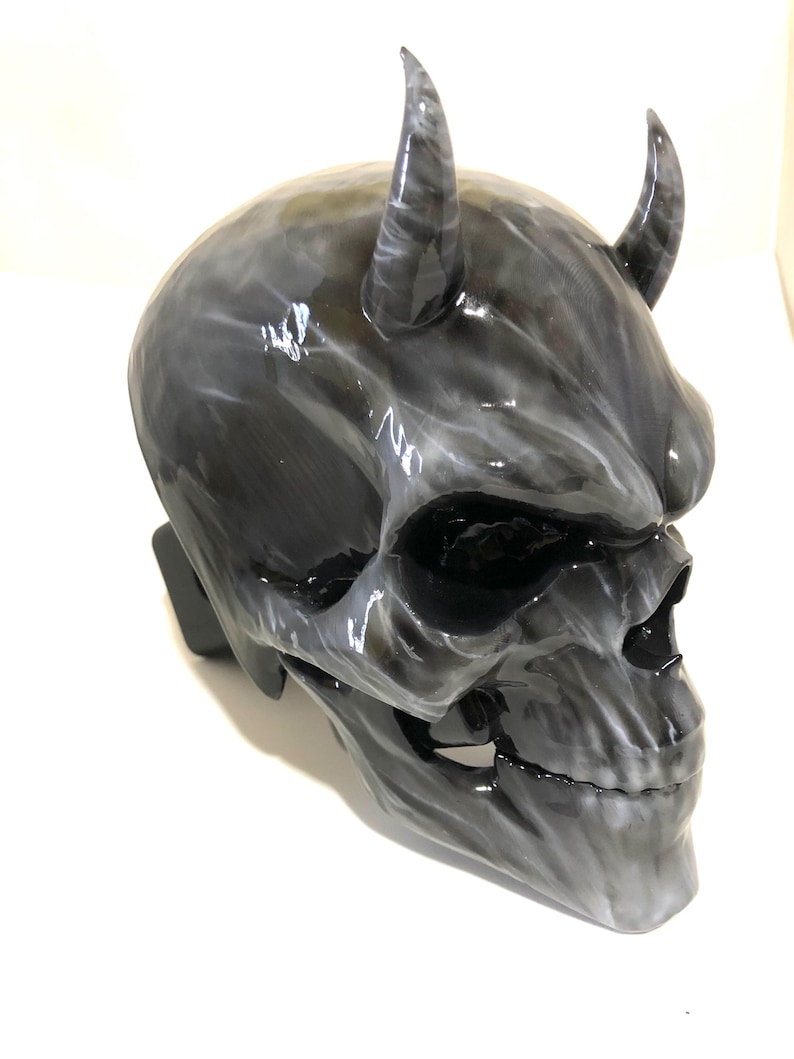 May include: A black and white skull mask with horns. The mask is made of a smooth, glossy material and has a detailed design.