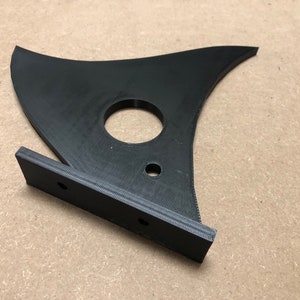 May include: A black plastic 3D printed object with a curved shape and a circular hole in the center. The object has a flat base with two holes on each side.