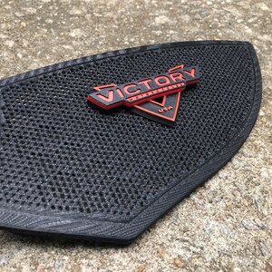 Puede incluir: Almohadilla de asiento de motocicleta negra con un logotipo de Victory Motorcycles rojo y negro.