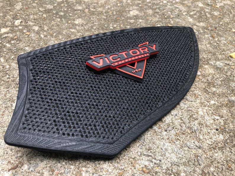 Puede incluir: Almohadilla de asiento de motocicleta negra con un logotipo de Victory Motorcycles rojo y negro.