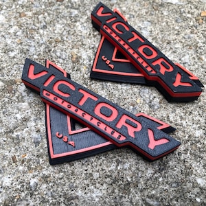 May include: Two black and red 3D printed emblems with the text "VICTORY MOTORCYCLES USA" on them.