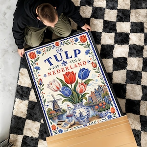 May include: A rectangular framed poster featuring the text DE TULP NEDERLAND. The illustration displays a bouquet of red, white, and blue tulips in a blue and white vase, a windmill, a sailboat, canal houses, and wooden clogs, all bordered by floral motifs.