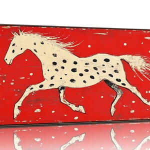 May include: A framed canvas print featuring a white horse with black spots galloping across a red background. The horse has a flowing mane and tail. The artwork has a rustic, distressed look.