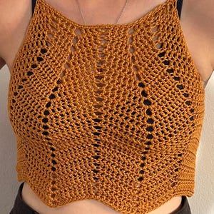 Peut inclure: Haut en crochet jaune moutarde avec un ourlet festonné. Le haut fait main présente une encolure halter et un motif ajouré détaillé. Le haut est sans manches, parfait pour le temps chaud. Le motif de crochet complexe ajoute une texture unique et un intérêt visuel au vêtement.