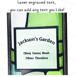May include: A rectangular, laser-engraved glass panel with the text "Jackson's Garden" and names: Olivia, Emma, Noah, Oliver, and Theodore. The panel has a white background with green and black geometric designs. The text "laser engraved text, you can add any text you like!" is at the top.