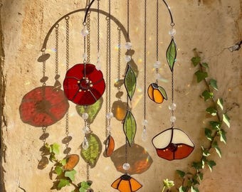 May include: A stained glass mobile featuring a semi-circular metal frame with hanging chains. The mobile includes red, orange, and white glass flower and leaf shapes interspersed with clear crystal beads that cast light reflections.