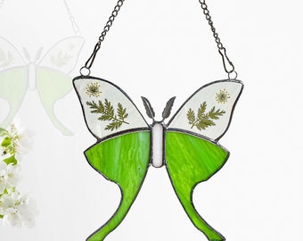 May include: A stained glass butterfly suncatcher with a green and white design. The butterfly has real pressed flowers and leaves incorporated into the design.
