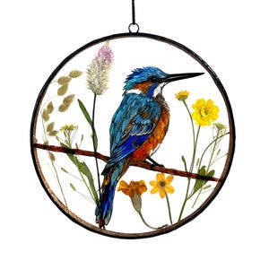 May include: A round, framed artwork featuring a blue and orange kingfisher perched on a branch with dried flowers. The flowers are yellow, pink, and white.