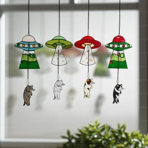 May include: Four hanging stained glass UFO wind chimes. Each UFO has a different color scheme: blue and white, green, red, and red and green. Each UFO has a cat holding a fish suspended below it. The cats are different colors.