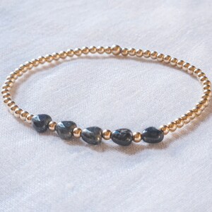 May include: A gold beaded bracelet with five dark blue gemstone beads.