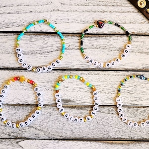 May include: Five beaded bracelets with different colored beads and white letter beads spelling out the phrases "Dance Dance", "Sugar Were Going Down", "This Aint A Scene", "Fall Out Boy", and "Thanks For The Mmms".