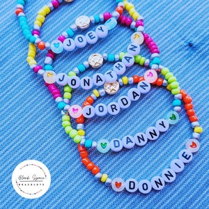 以下が含まれることがあります： 異なる名前が書かれたカラフルなビーズブレスレットが5つあります。名前はジョーイ、ジョナサン、ジョーダン、ダニー、ドニーです。各ブレスレットにはハートのチャームと星のチャームが付いています。