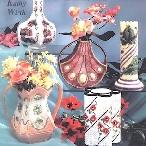 以下が含まれることがあります： 9つの花瓶のデザインを特集したプラスチックキャンバスのクラフトプロジェクトの書籍カバー。表紙には、バラ、蘭、デイジーなど、さまざまな花瓶と花のアレンジメントが描かれています。本のタイトルは「Vases」、サブタイトルは「9 Designs in 10-Mesh」。著者はキャシー・ワースです。