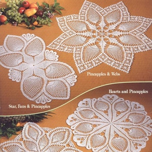 May include: Four white crocheted doilies with different patterns, including pineapples, stars, and hearts. The doilies are on a brown background with pears and grapes.