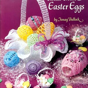 May include: A crochet Easter egg basket with a white handle and pink, yellow, blue, and green crocheted eggs. The basket is filled with white crocheted flowers and a pink ribbon. The eggs are decorated with small white flowers. The basket is sitting on a pink surface with white and pink confetti.