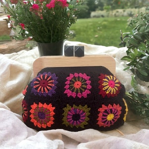 Può includere: Una pochette a uncinetto con cornice in legno e motivi floreali neri, arancioni, rosa, verdi e gialli.