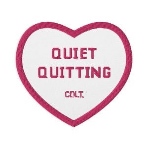 Può includere: Una toppa a forma di cuore rosa con ricamo bianco che dice "Quiet Quitting" e "COLT."