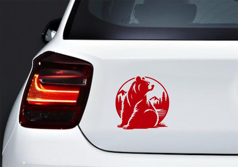 May include: Red bear silhouette sticker on a white car. The sticker features a bear sitting in front of a mountain and forest scene, enclosed in a circular frame. The design is a simple, bold graphic.