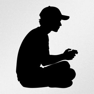Puede incluir: Una silueta negra de una persona con gorra de béisbol, sentada con las piernas cruzadas mientras sostiene un mando de videojuegos. La figura se muestra de perfil, orientada hacia el lado derecho del encuadre.