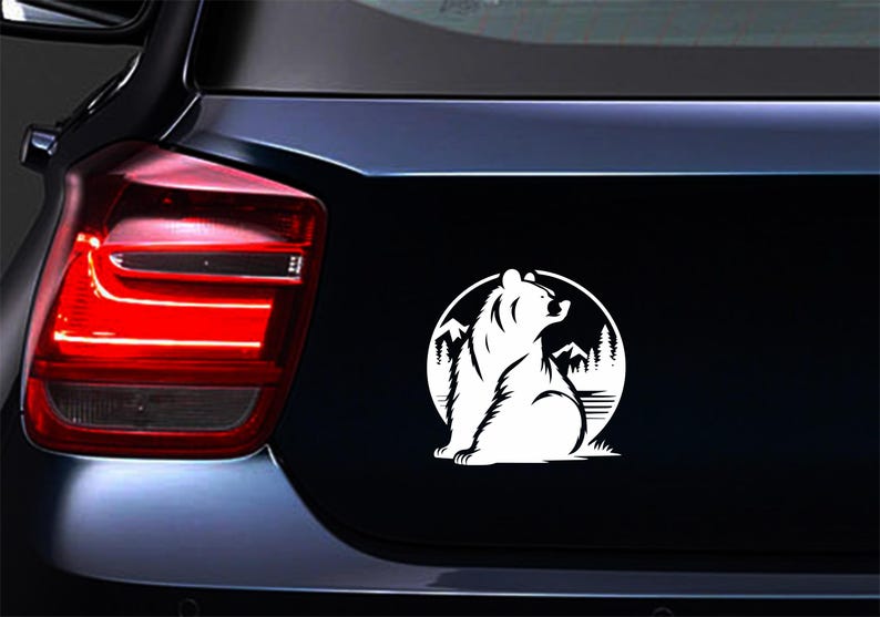 May include: White bear silhouette sticker on a black car surface. The bear is inside a circle with mountain and tree details. The sticker is likely for a car or vehicle.