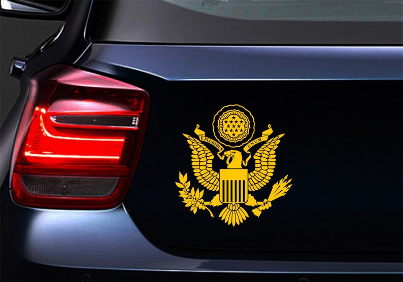 Pode incluir: Um adesivo dourado do Grande Selo dos Estados Unidos, com uma &aacute;guia de asas abertas, um escudo com listras verticais e uma faixa que diz "E PLURIBUS UNUM".