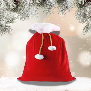 May include: A large red velvet Santa Claus gift bag with a white fluffy top and gold drawstring closure. The bag has white pom-poms at the end of the drawstrings. The background has a blurred effect with snowy pine branches.