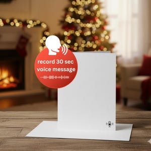 May include: A white greeting card with a microphone icon and the text "record 30 sec voice message" on a red circle. The card is on a wooden surface with a Christmas tree and fireplace in the background.