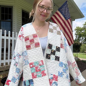 May include: A quilted jacket featuring a patchwork design with a white base and various colorful fabric squares in shades of red, blue, green, and black. The garment has an open front, long sleeves, and a diamond-stitched texture throughout the fabric.