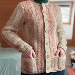Peut inclure: Cardigan tricoté beige et rouge avec une fermeture boutonnée et deux poches avant. Le cardigan présente des rayures verticales en tricot beige et rouge. Les manches sont longues et le col est un col roulé vert foncé.
