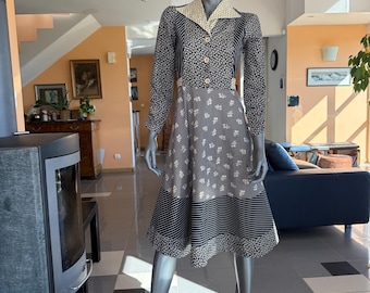 May include: A long-sleeved midi dress featuring a mix of black and white patterns, including floral prints and thin vertical stripes. The dress has a collared neckline, a button-down front with three visible buttons, and a flared skirt design.