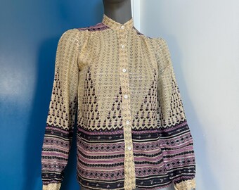 May include: A long-sleeved button-down shirt featuring a beige base with a repeating pattern of small dark hearts, horizontal stripes, and geometric shapes in shades of black, purple, and metallic gold thread woven throughout the fabric.