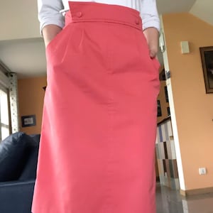 Puede incluir: Una falda rosa coral de cintura alta con cierre de botón. La falda tiene bolsillos a los lados y llega hasta la rodilla.