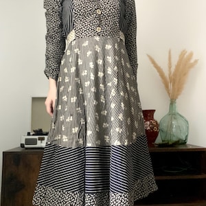 Peut inclure: Une robe à manches longues à motifs noirs et blancs avec un devant boutonné. La robe a un design patchwork avec différents motifs floraux et rayés.