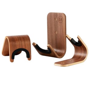 May include: Three wooden guitar wall hangers with a curved design. The hangers are made of a dark wood with a black rubber cradle. The hangers are designed to hold a guitar and are mounted on a wall.